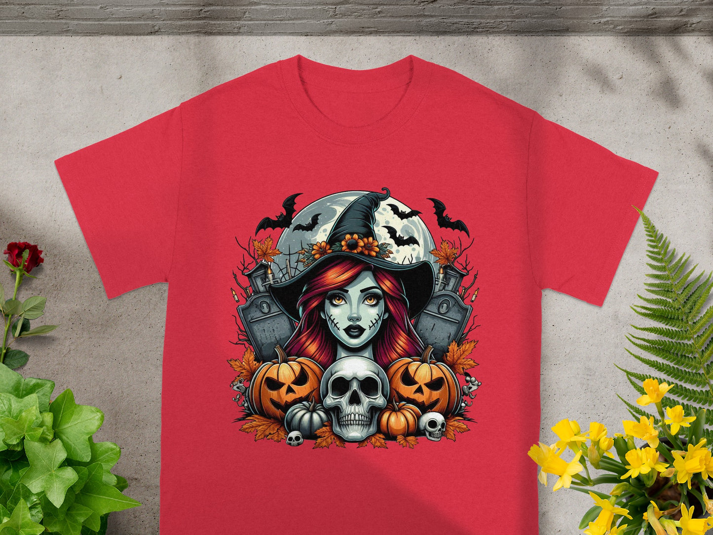 Halloween graphic of a witch, skull, pumpkins, bats, and tombstones on a red t-shirt.