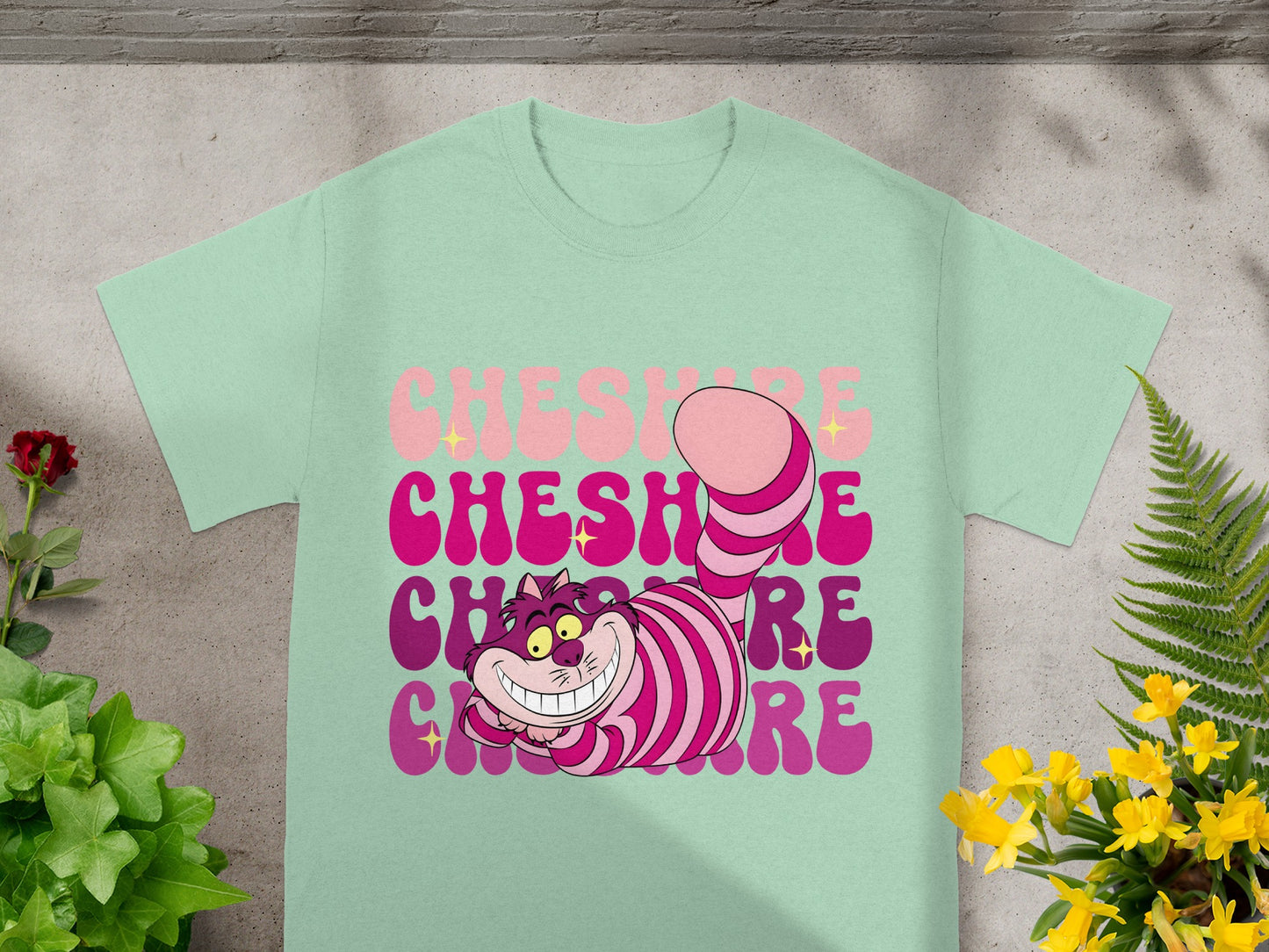 Mint green t-shirt with a pink and purple striped Cheshire Cat and "Cheshire Cat" text.