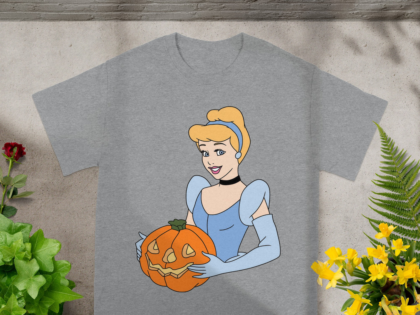 Cinderella holding a jack-o'-lantern on a gray t-shirt with decorative plants.
