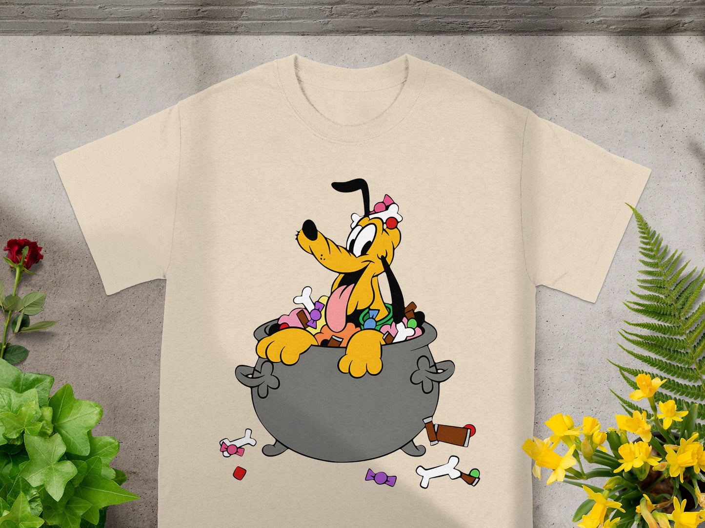 Pluto in a cauldron filled with candy, Halloween themed graphic on a tan t-shirt.