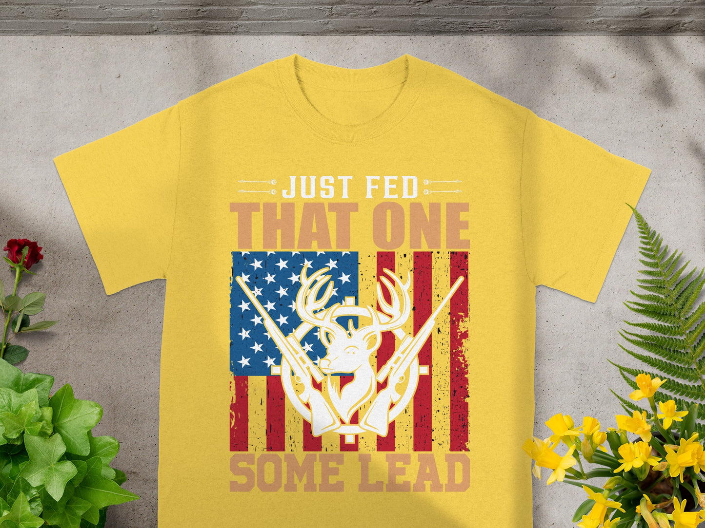 Yellow t-shirt with text "JUST FED THAT ONE SOME LEAD" and deer skull with guns USA flag graphic.