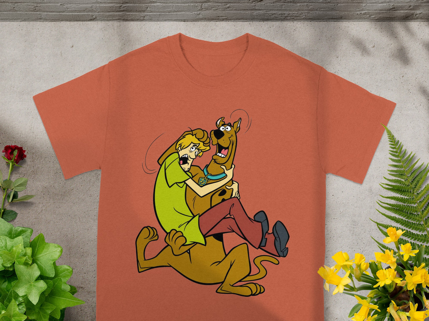 Scooby-Doo and Shaggy embrace in a playful cartoon scene on an orange t-shirt.