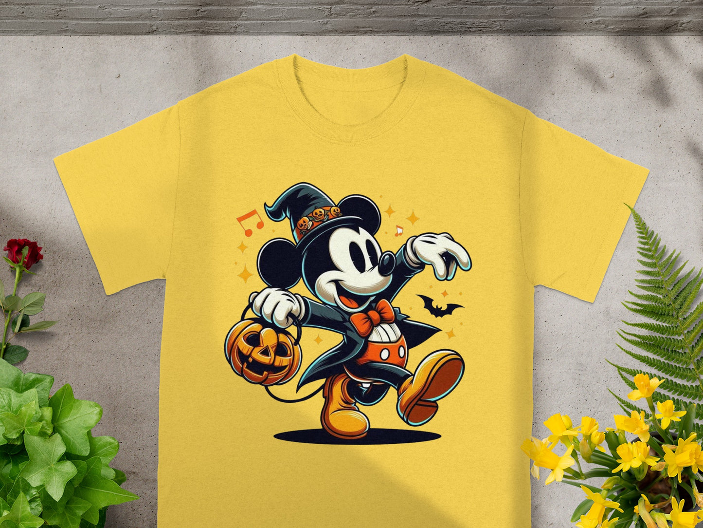 Mickey Mouse in a witch hat holding a pumpkin bucket, on a yellow t-shirt.