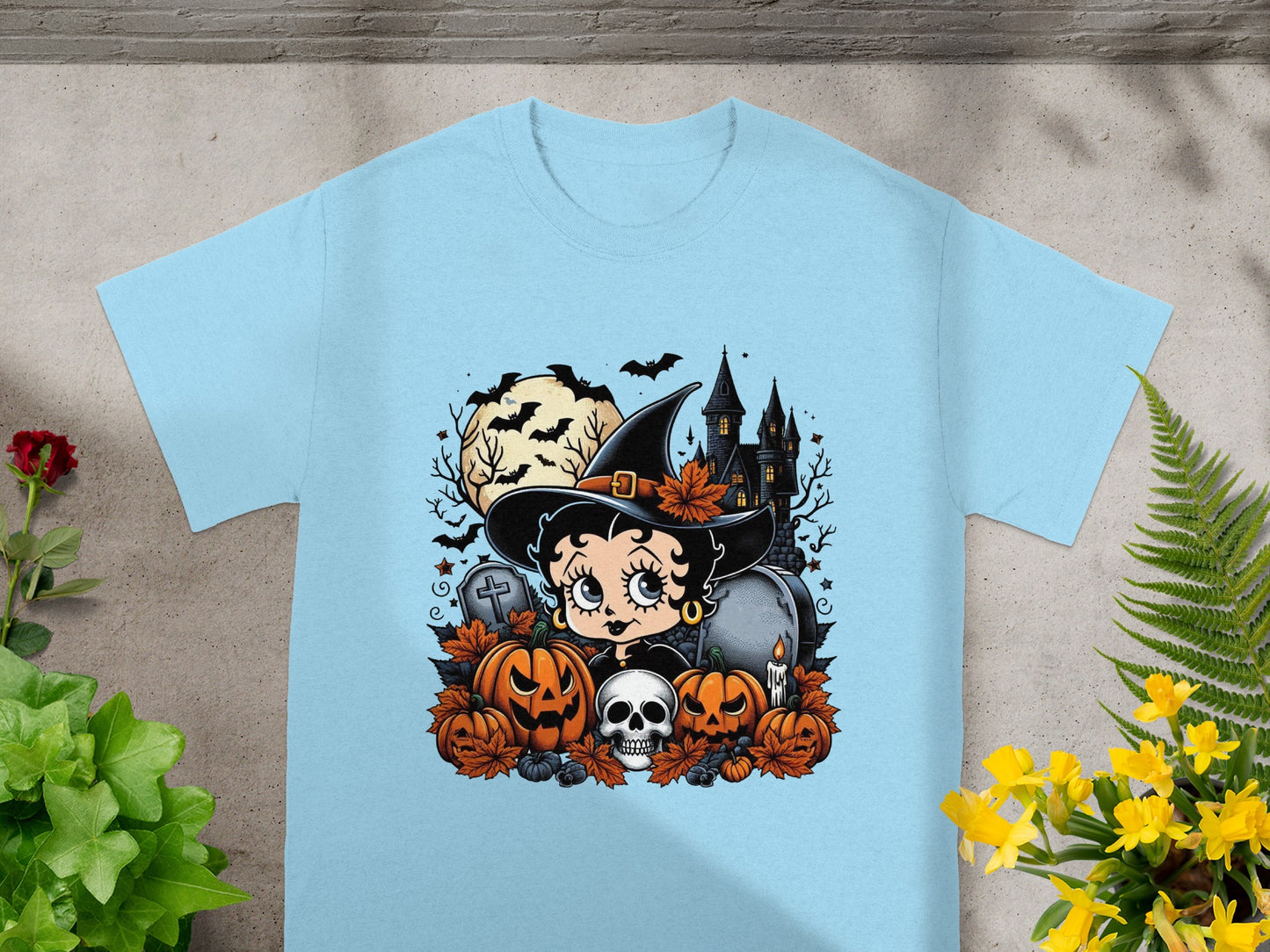 Betty Boop as a witch with pumpkins, skull, and haunted castle on a light blue t-shirt.