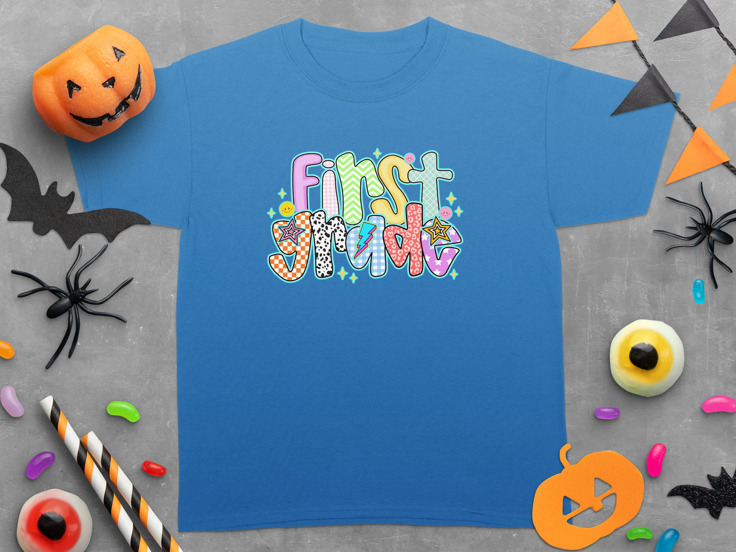 Blue t-shirt with "First Grade" text featuring colorful patterns and Halloween decorations.