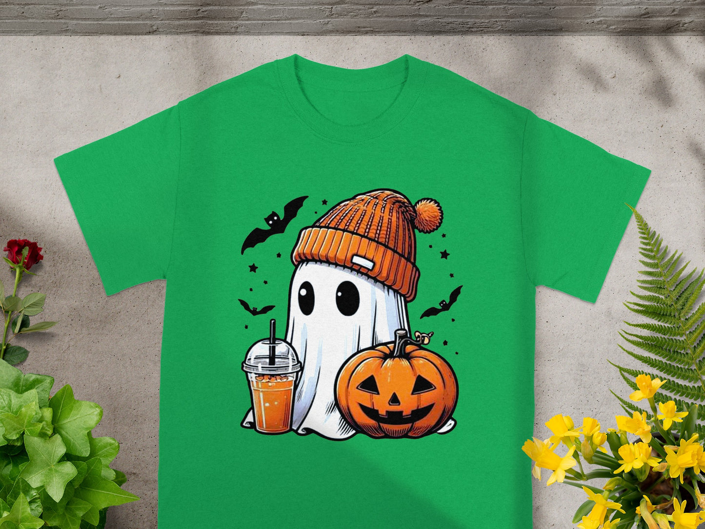 Green t-shirt with a cartoon ghost wearing an orange beanie next to a pumpkin and drink.