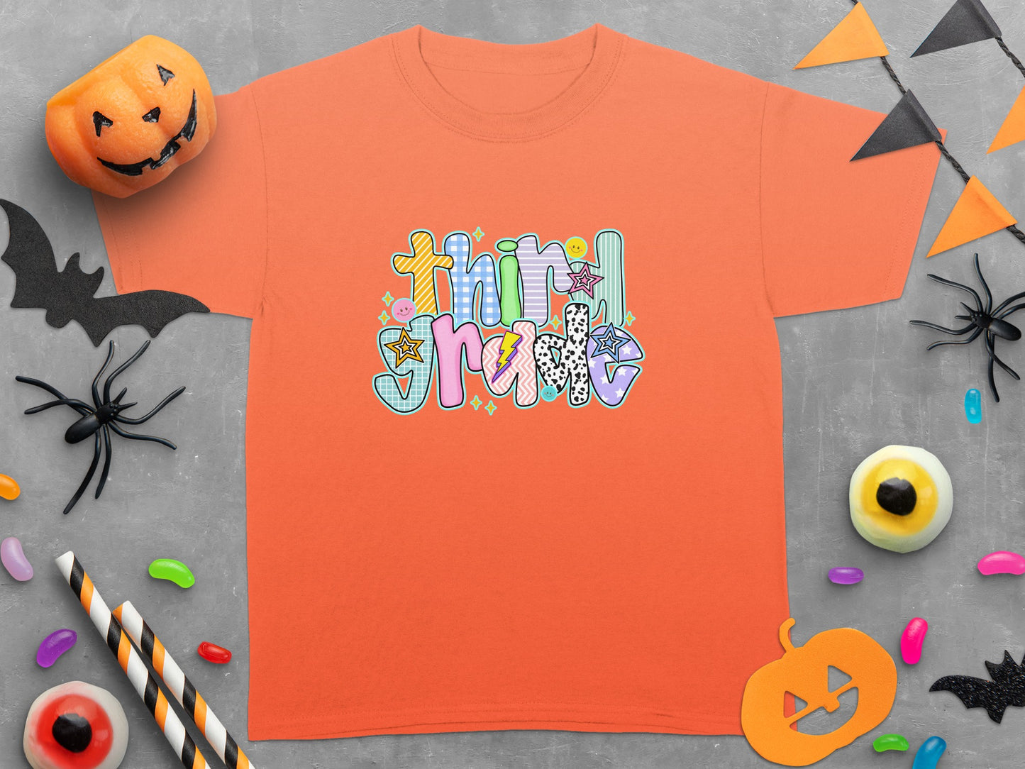 Orange t-shirt with "Third Grade" in colorful, textured lettering surrounded by Halloween decorations.