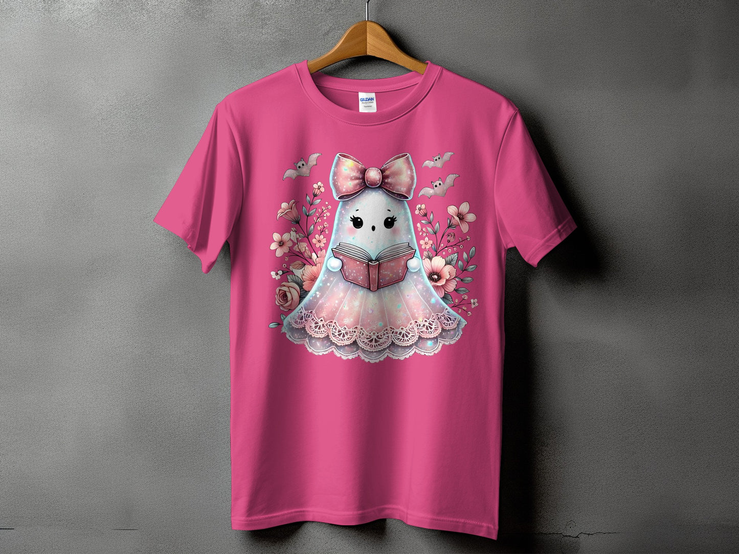 Pink t-shirt with a kawaii ghost reading a book surrounded by flowers and bats.