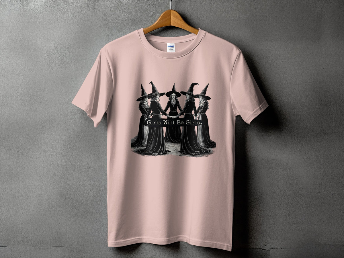 Pink t-shirt with a graphic of five witches holding hands and the text "Girls Will Be Girls."