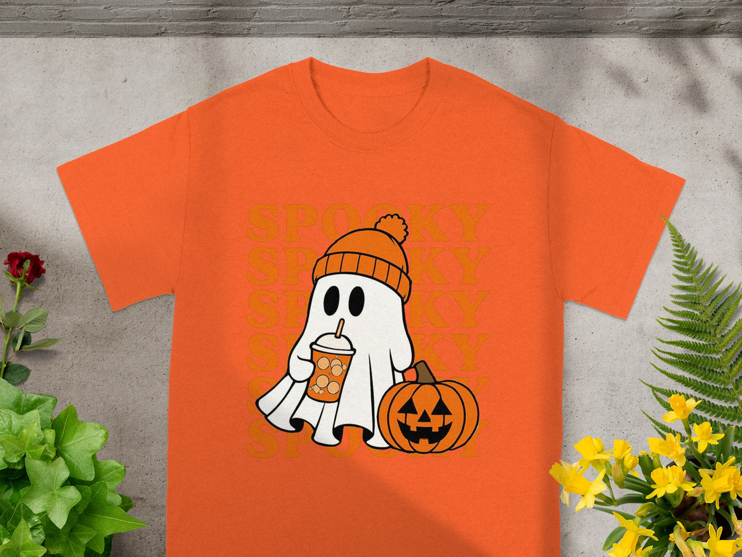 Orange t-shirt with cartoon ghost holding drink next to pumpkin.