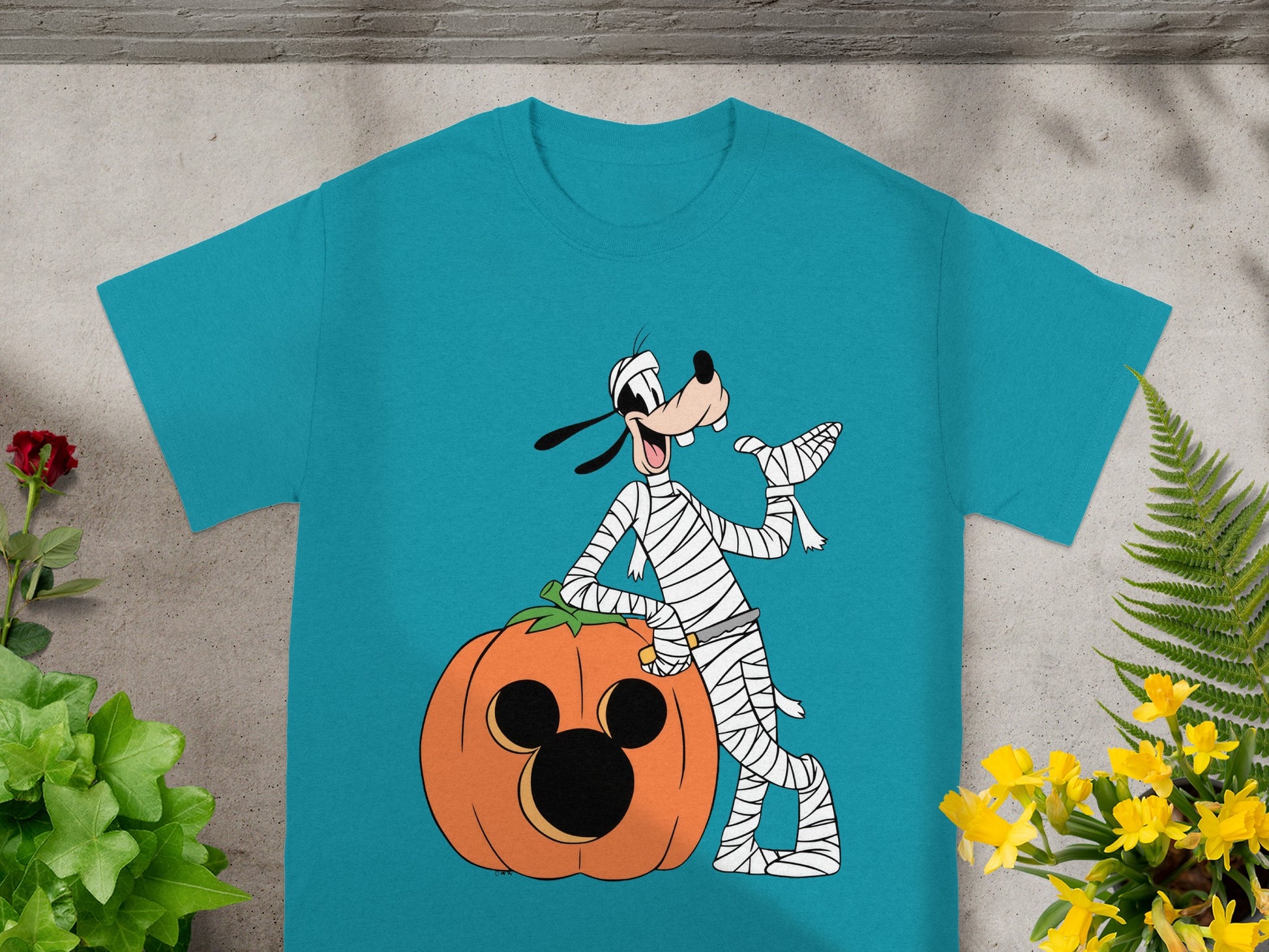 Mummy Goofy leans on a Halloween pumpkin with Mickey Mouse ears.