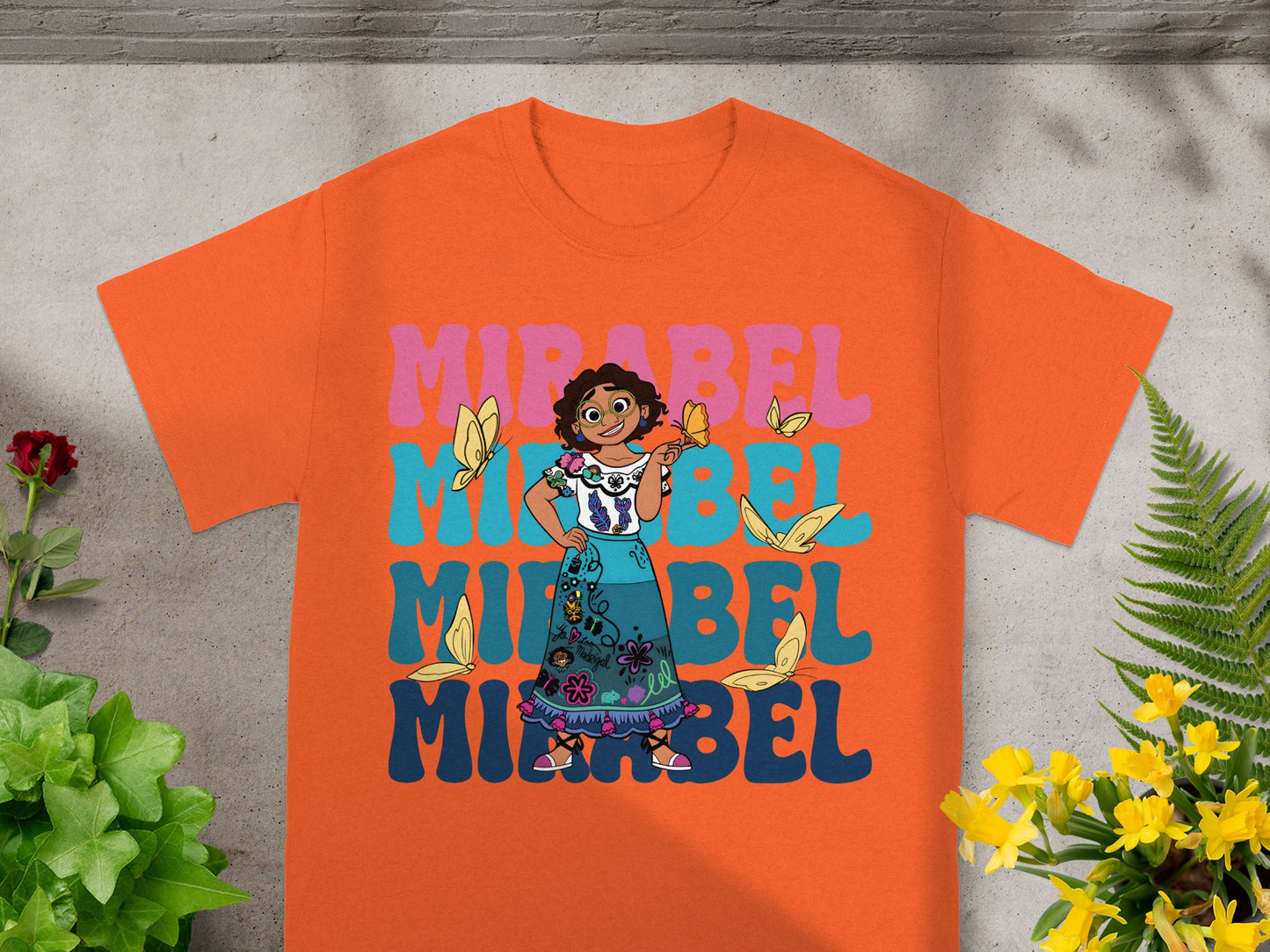 Orange t-shirt with Mirabel from Encanto and colorful text.