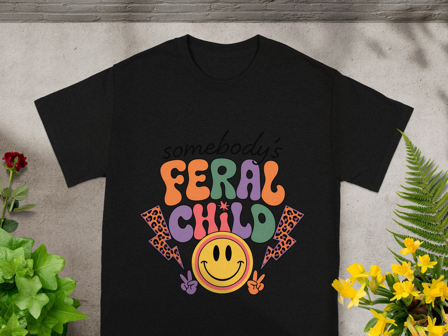 Black t-shirt with "somebody's FERAL CHILD" text, smiley face, and lightning bolts.