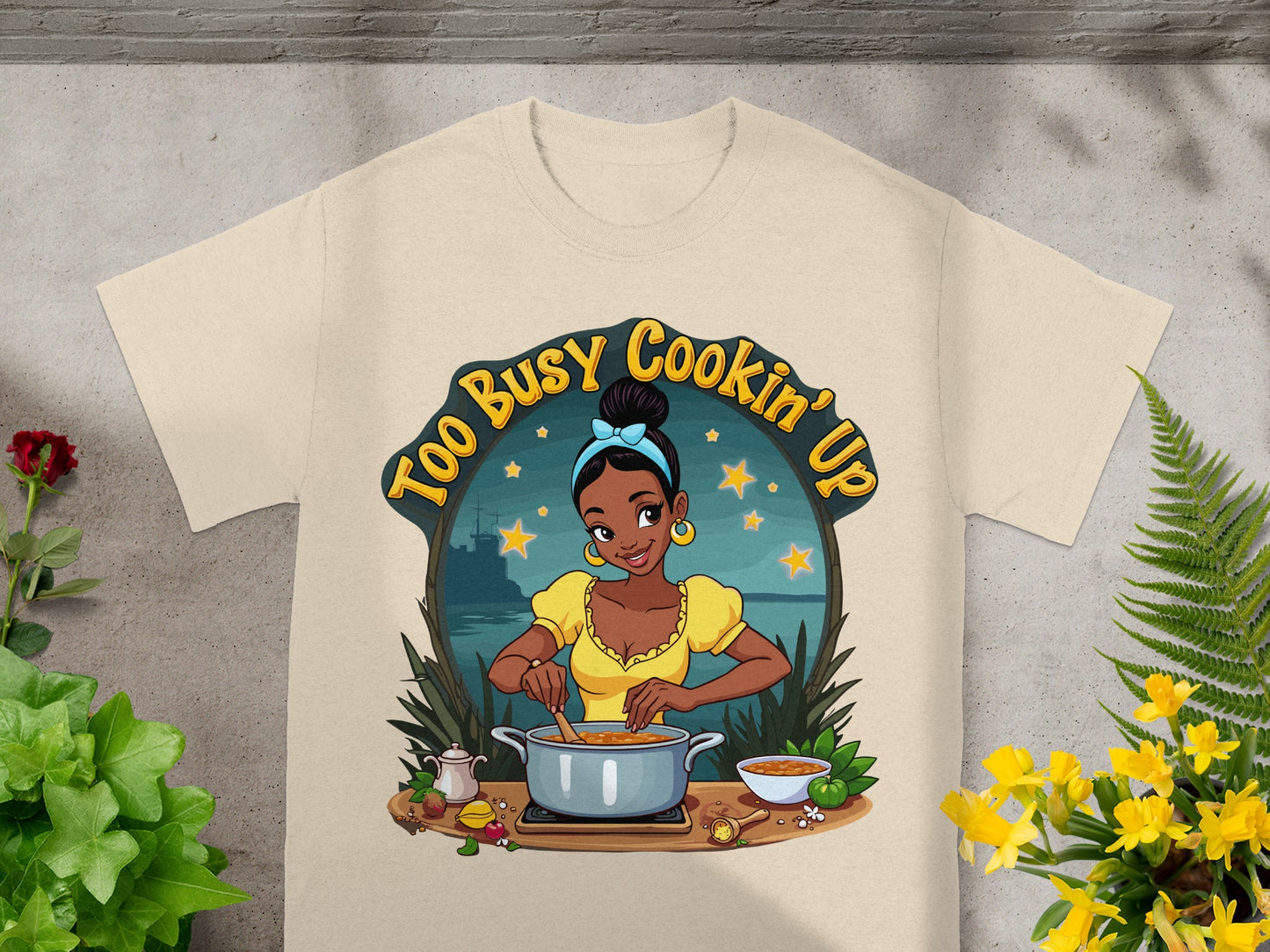 Cream t-shirt with a woman cooking and text "Too Busy Cookin' Up".