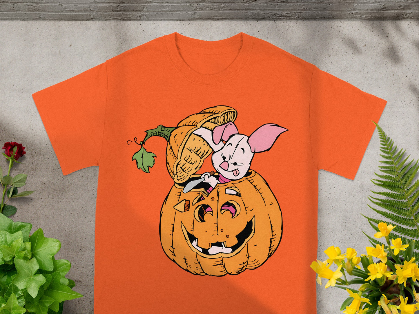 Piglet peeking out of a jack-o'-lantern on an orange t-shirt.