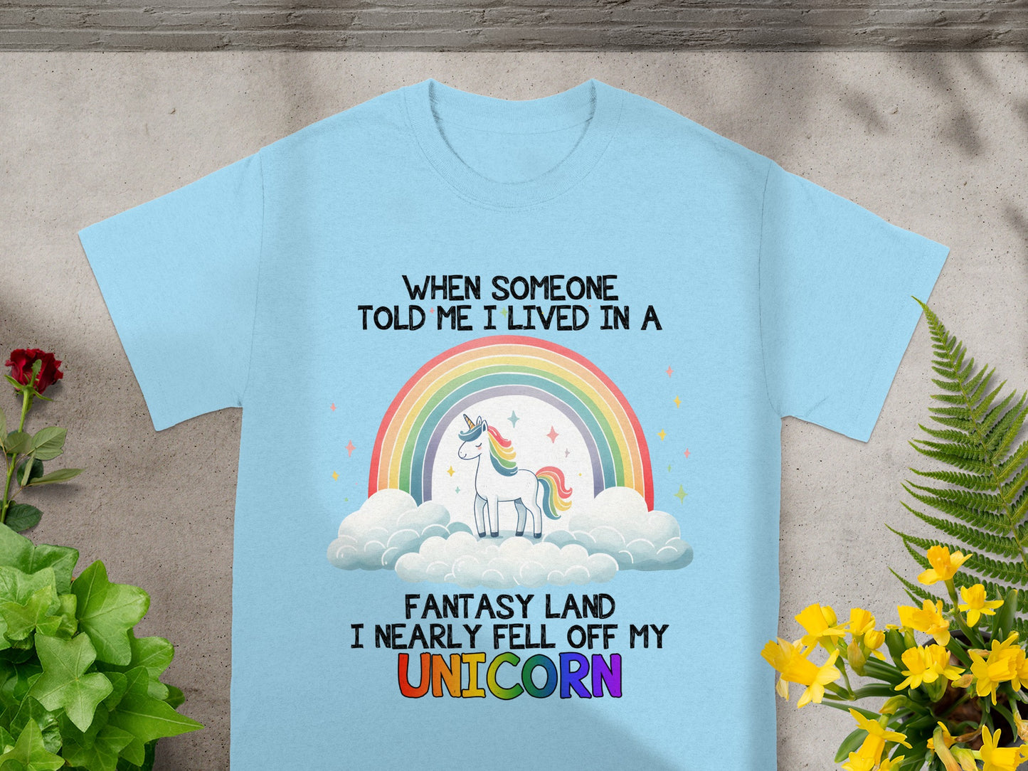 Light blue t-shirt with text and unicorn graphic on clouds with rainbow.