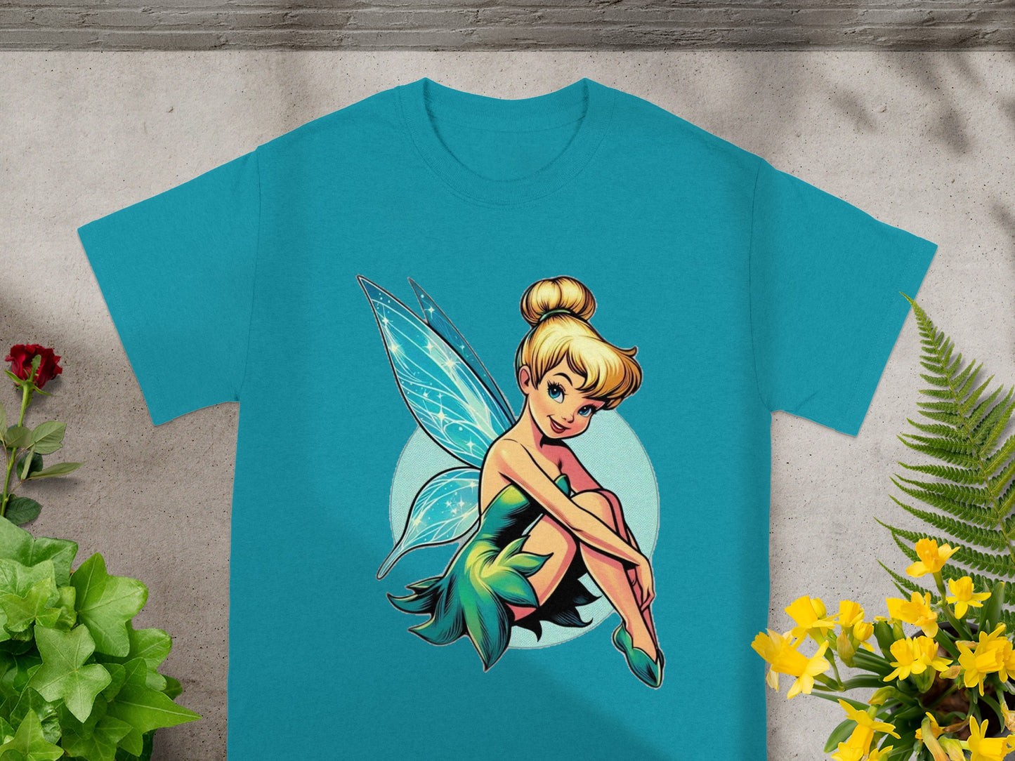 Tinkerbell sits cross-legged on a light blue circle on a teal t-shirt.