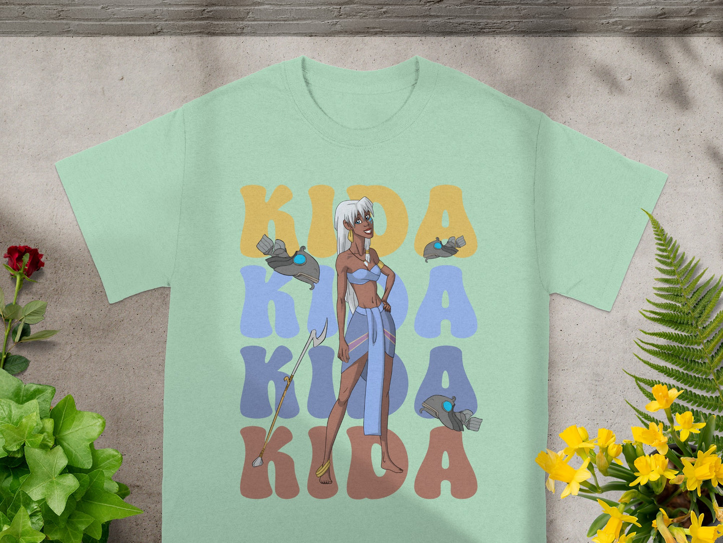 Light green t-shirt with "Kida Kida Kida" text and stylized Atlantis character.
