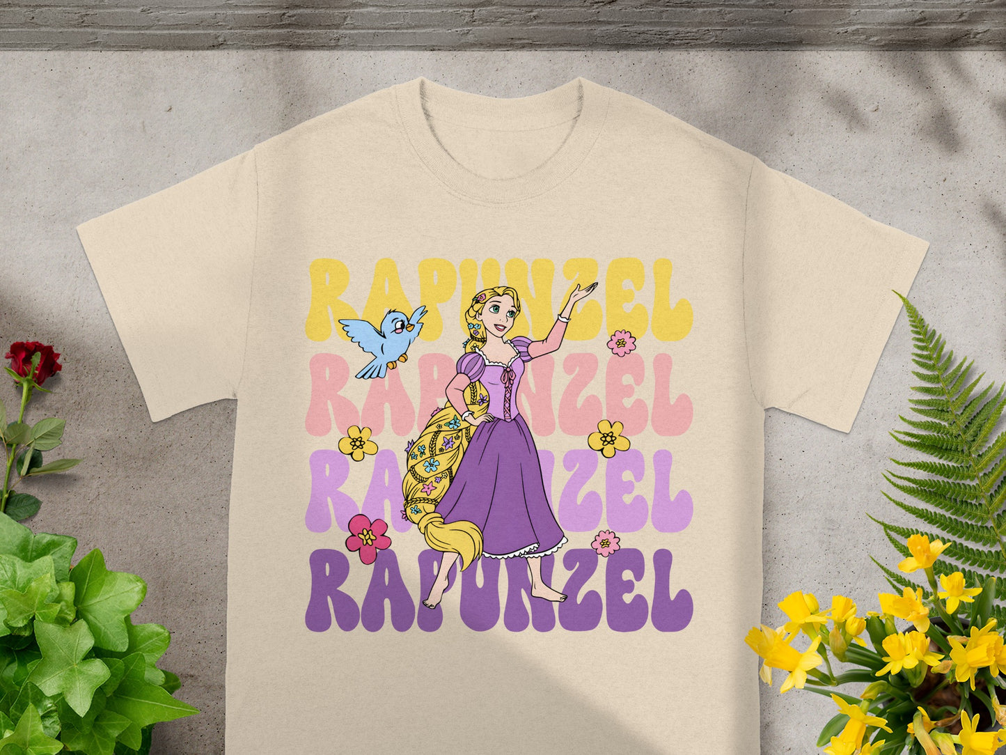Rapunzel graphic with bird and floral accents on a light cream t-shirt.