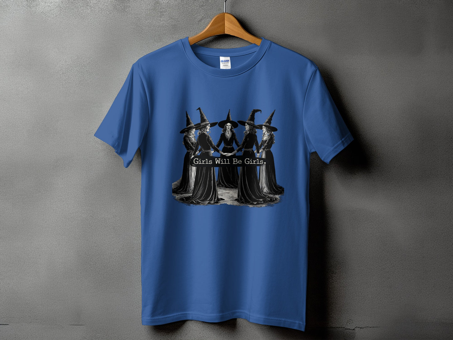Blue t-shirt with a graphic of witches holding hands and the text "Girls Will Be Girls."