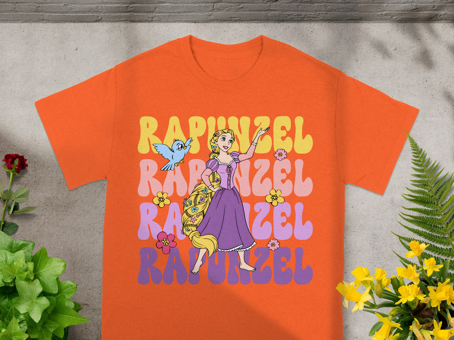 Orange t-shirt with Rapunzel and Pascal illustration and wavy text.