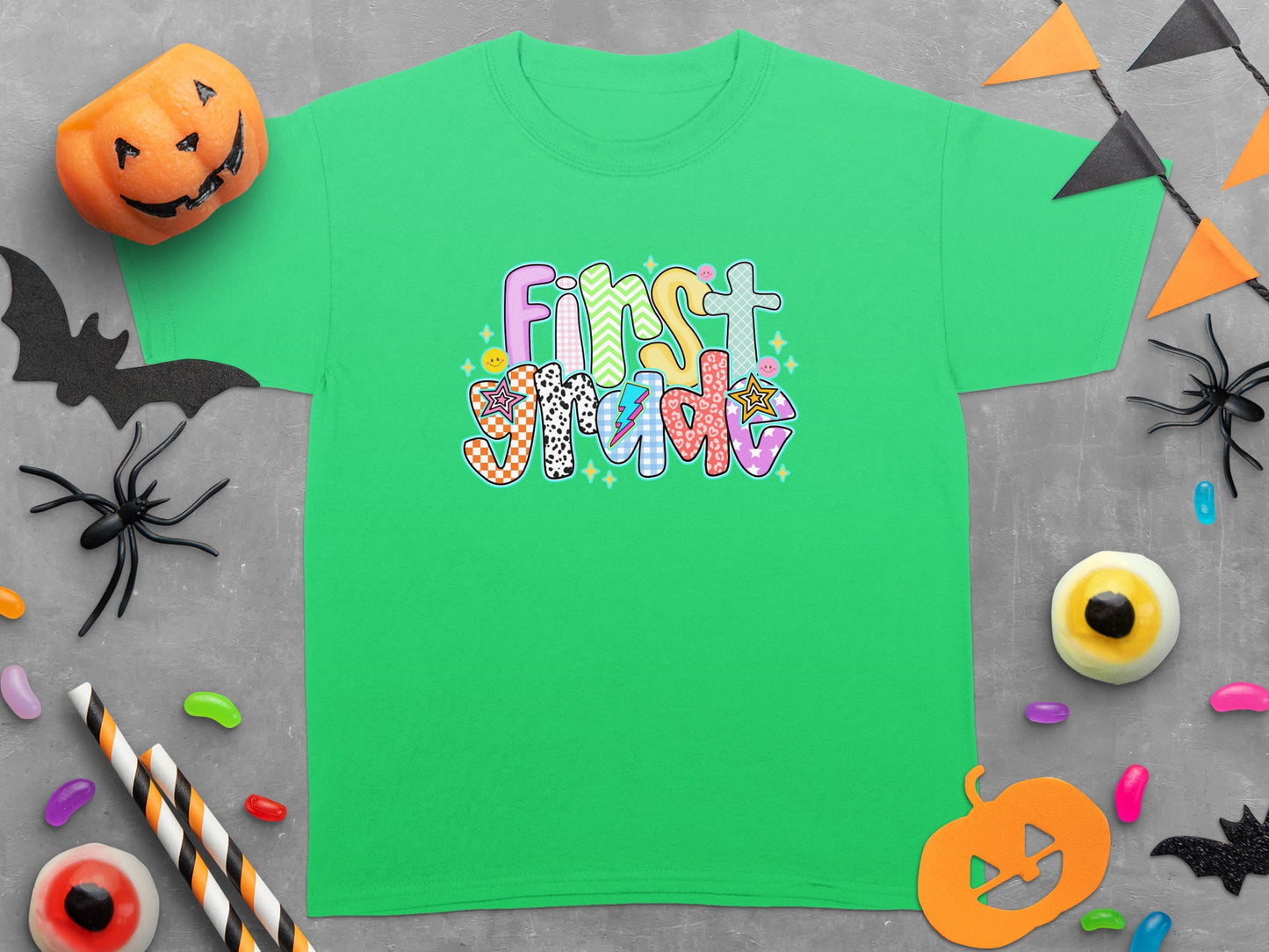 Green t-shirt with colorful "First Grade" Halloween themed graphic and surrounding decorations.