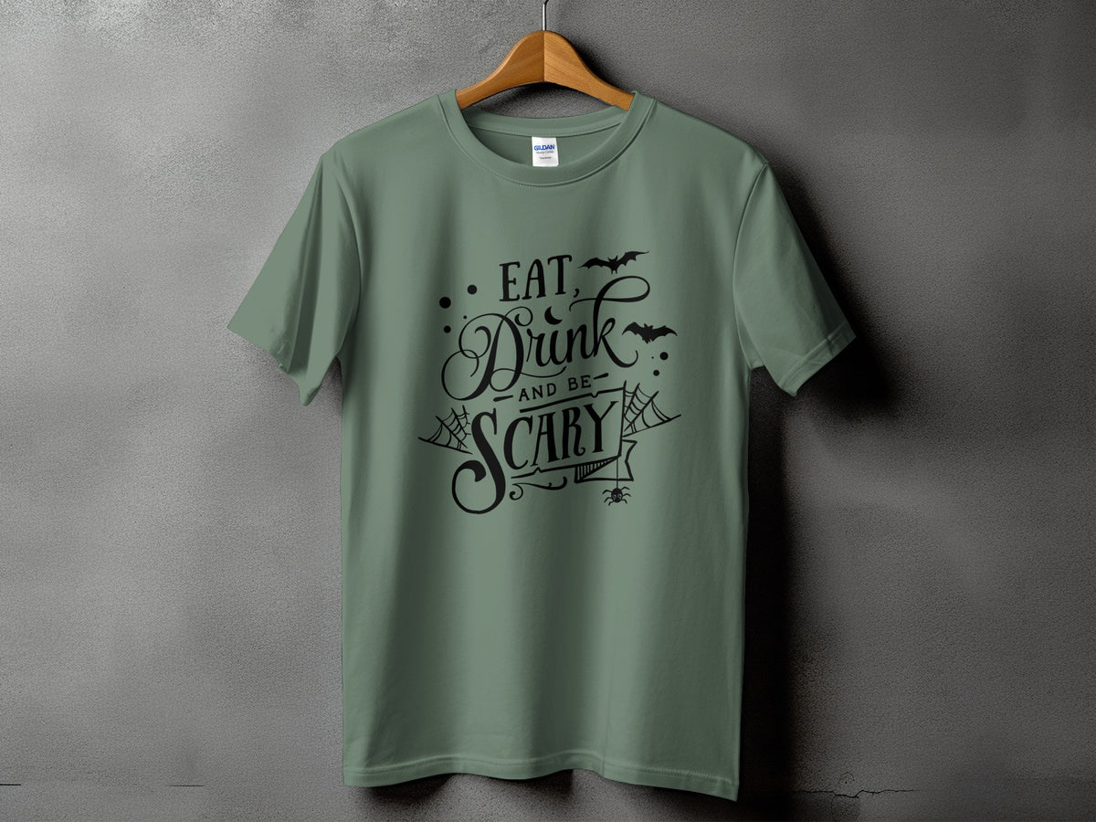 Sage green t-shirt with black text "Eat, Drink, and Be Scary" and Halloween graphics.