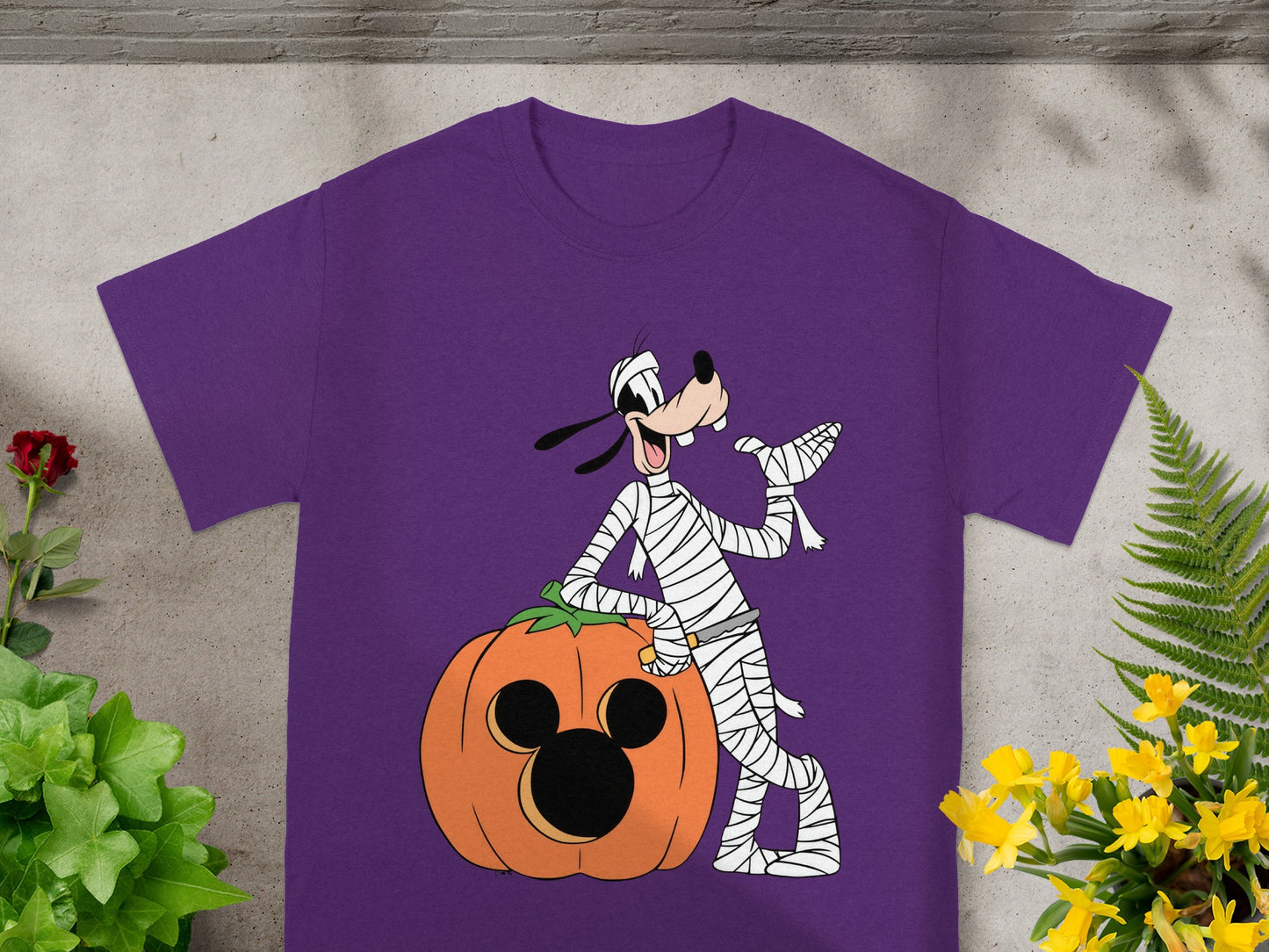 Purple t-shirt with Goofy dressed as a mummy next to a Mickey Mouse pumpkin.