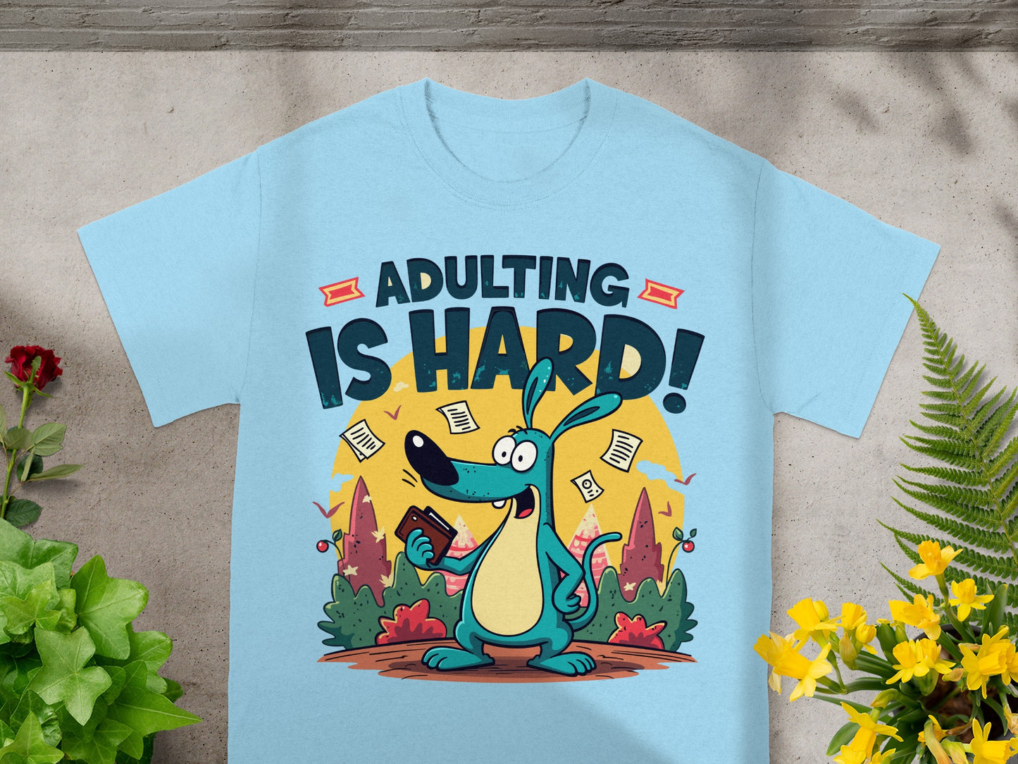 Light blue t-shirt featuring "ADULTING IS HARD!" text and cartoon dog holding a wallet, surrounded by papers.