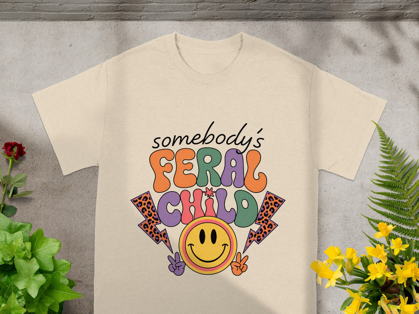 Light tan t-shirt with "Somebody's FERAL CHILD" text and smiley face.