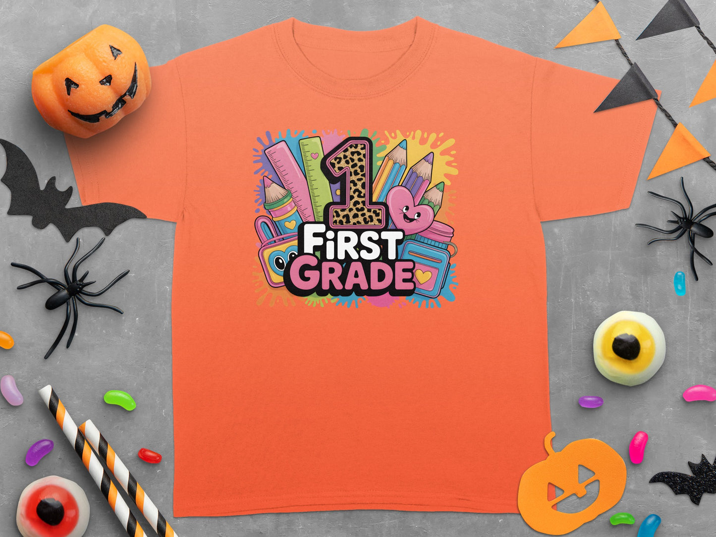 Orange t-shirt with "First Grade" graphic featuring school supplies and a heart.