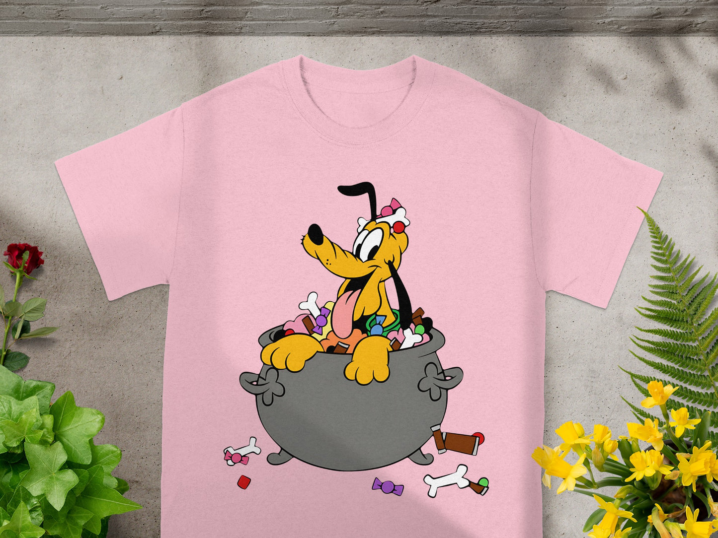 Pluto sits in a cauldron overflowing with Halloween candy on a pink t-shirt.