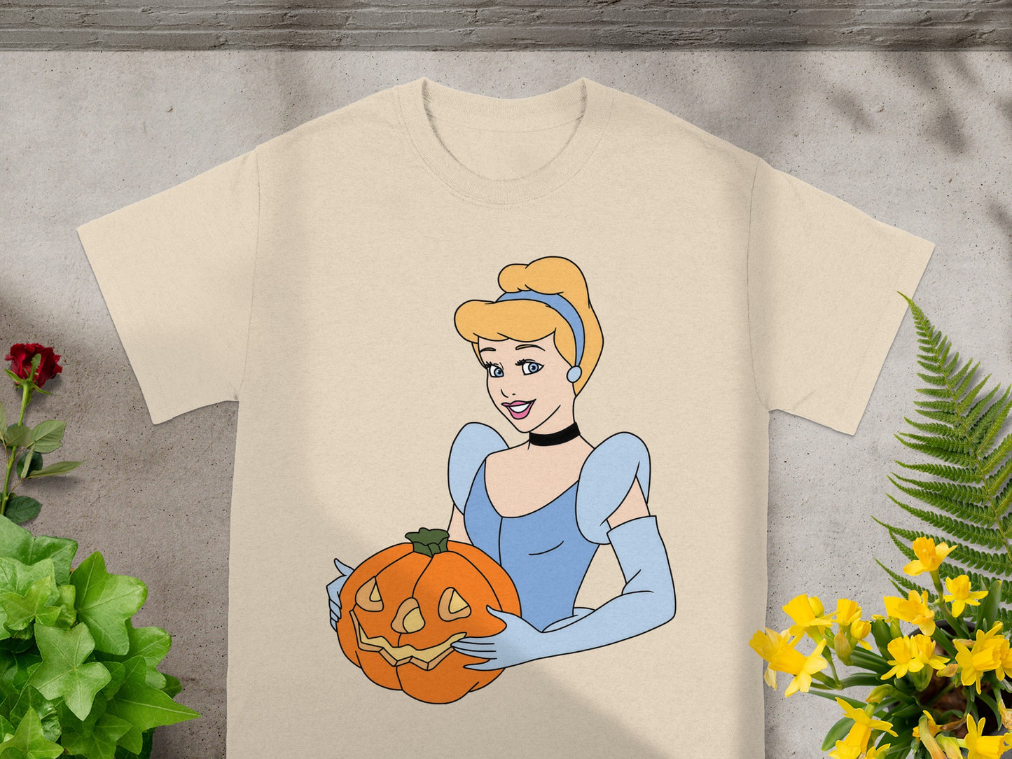 Cinderella wearing blue holds a jack-o'-lantern on a tan t-shirt.