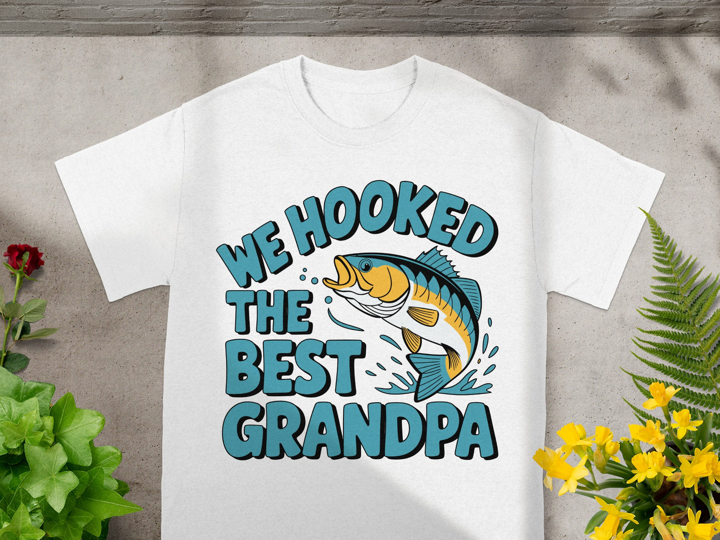 White t-shirt with text "WE HOOKED THE BEST GRANDPA" and a fish graphic.