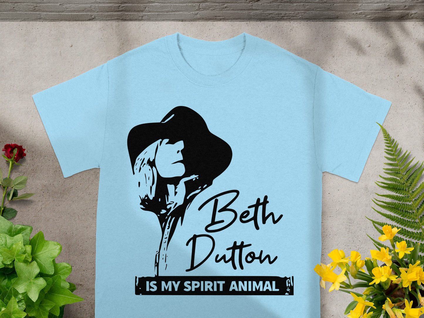 Light blue t-shirt with black graphic of Beth Dutton and text.