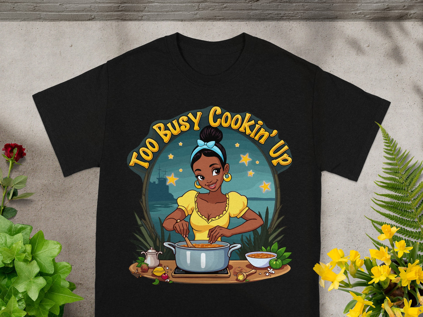 Black t-shirt with "Too Busy Cookin' Up" and cartoon woman cooking.