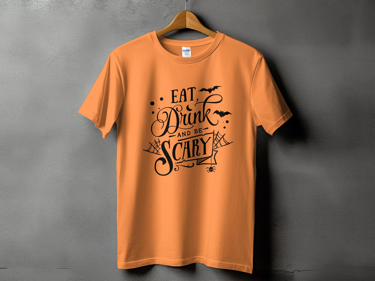 Orange t-shirt with black text "Eat, Drink, and Be Scary" with Halloween graphics.