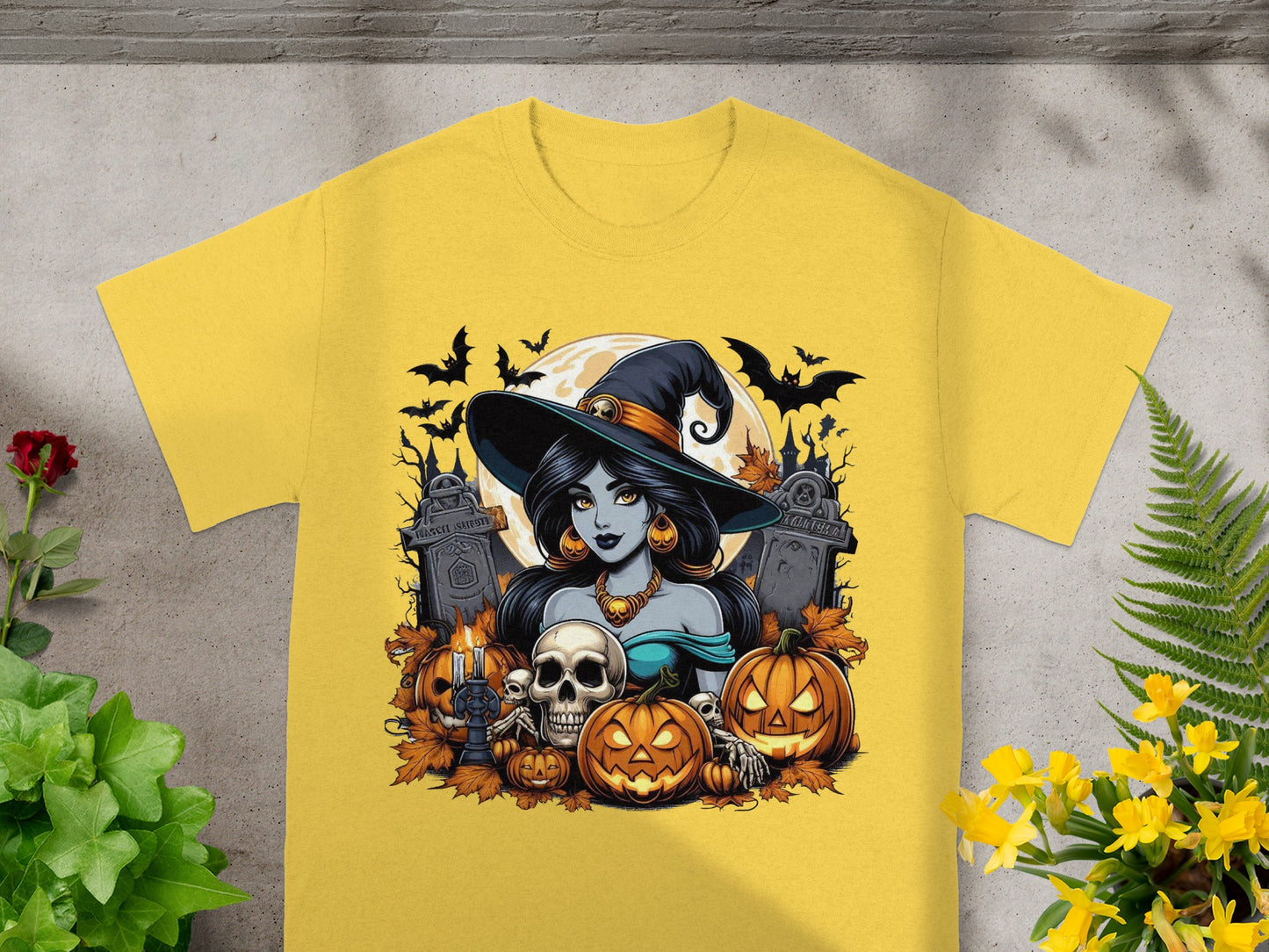 Halloween graphic with witch, pumpkins, skulls, bats, and tombstones on a yellow t-shirt.
