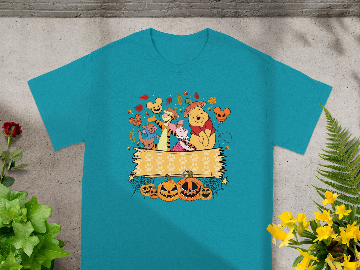 Winnie the Pooh characters with pumpkins and fall leaves on a teal t-shirt.