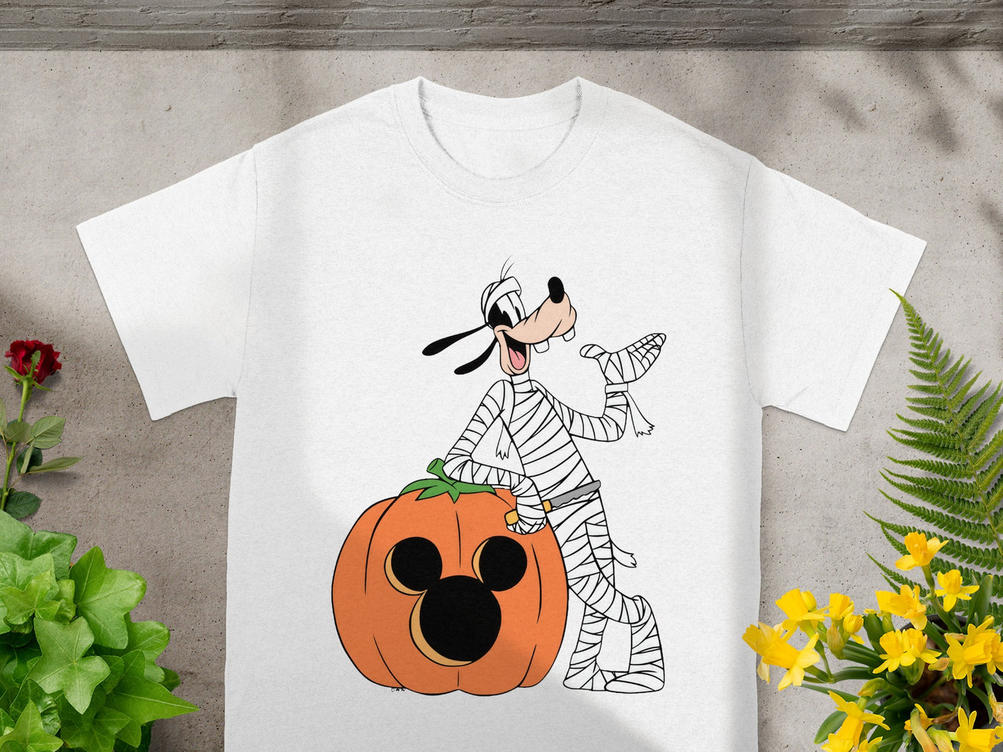 White t-shirt with cartoon Goofy as a mummy next to a Mickey Mouse pumpkin.