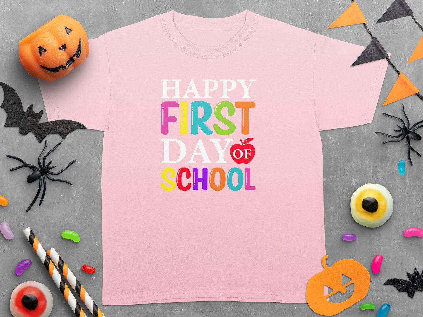 Pink t-shirt with "Happy First Day Of School" text and Halloween decor.