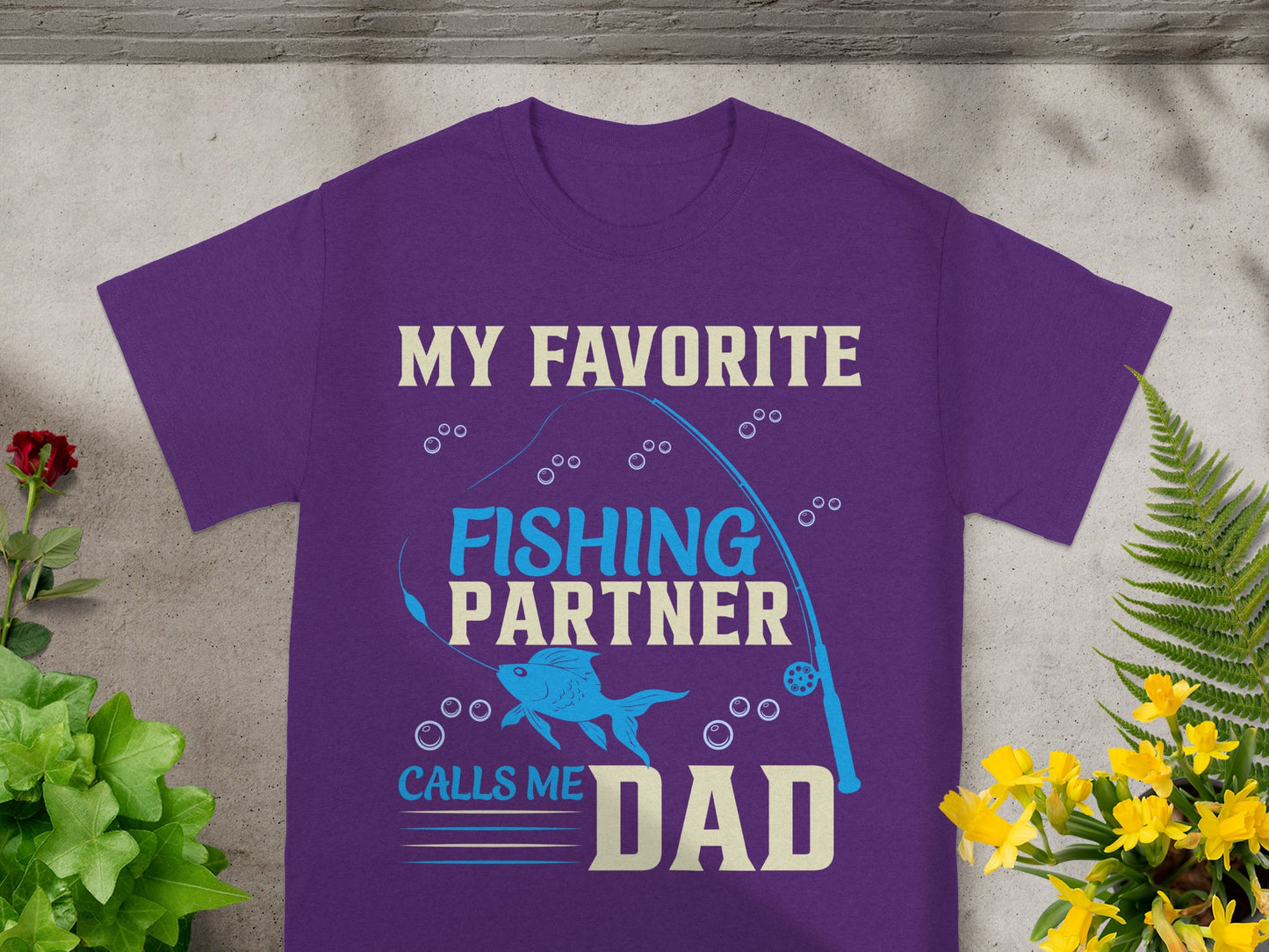 Purple t-shirt with text "MY FAVORITE FISHING PARTNER CALLS ME DAD" and fishing graphics.