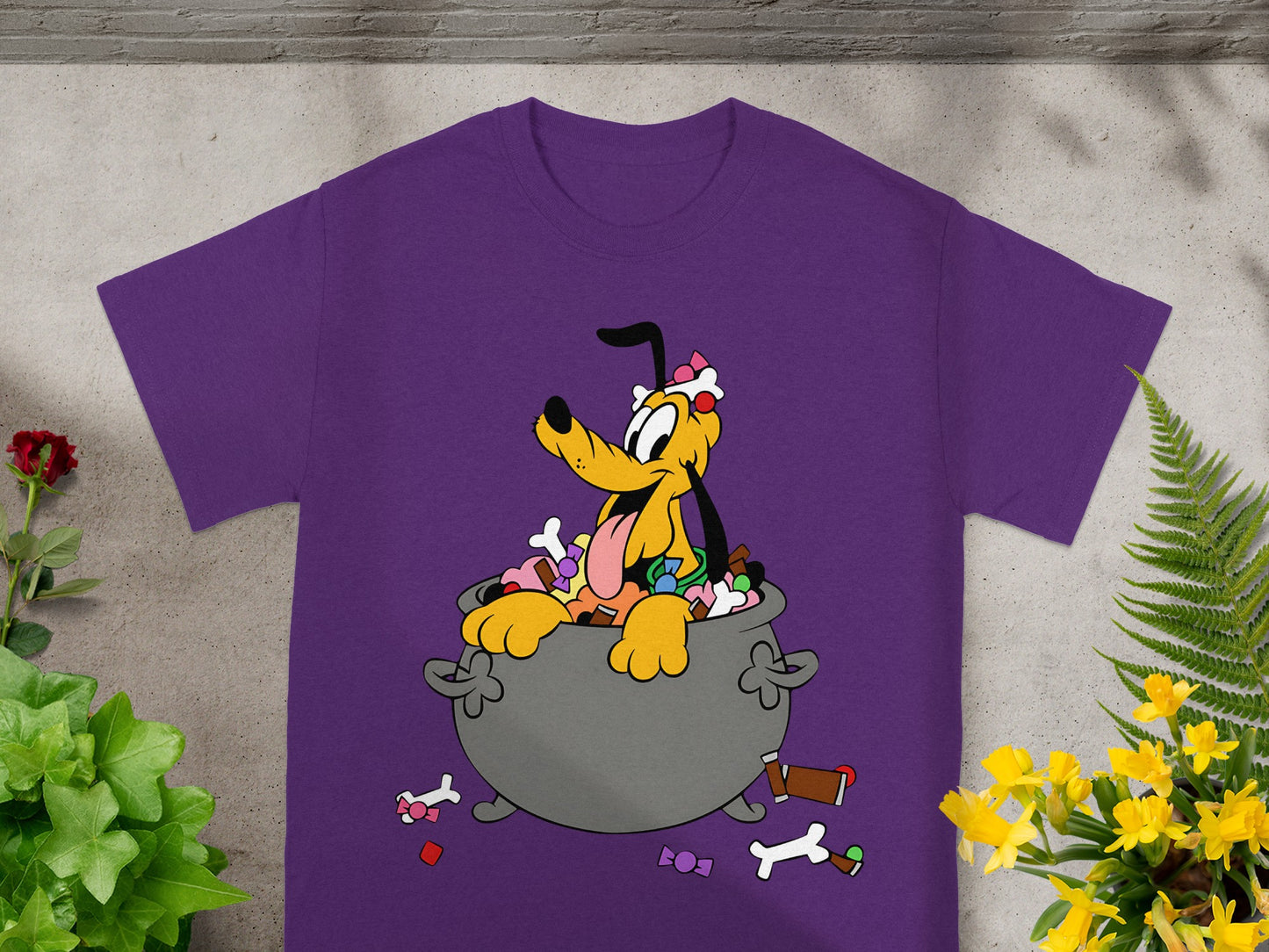 Pluto the dog sits in a cauldron filled with candy on a purple t-shirt.