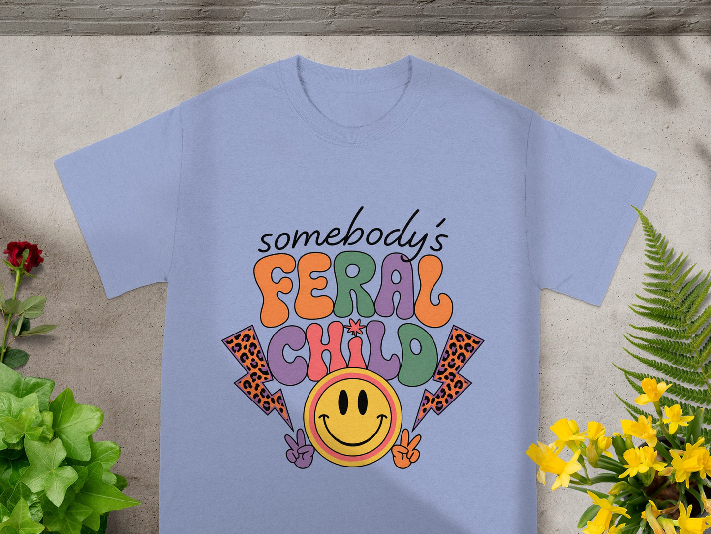 Light purple t-shirt graphic with retro text "somebody's FERAL CHILD" and smiley face.