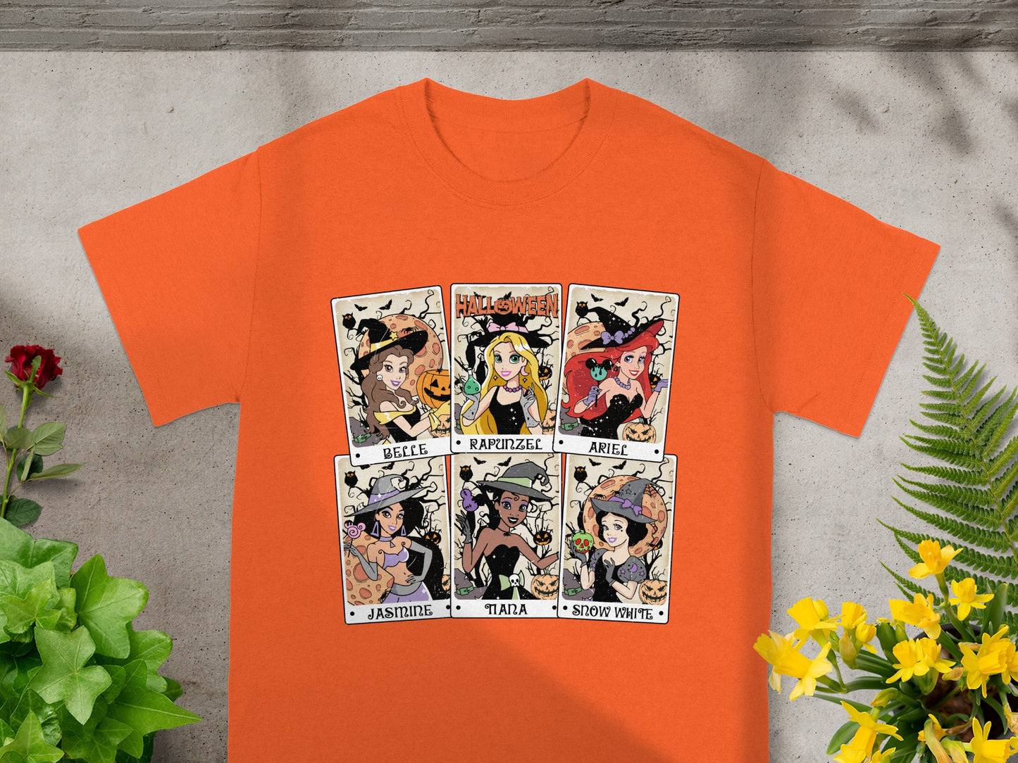 Orange t-shirt with six Halloween-themed princess portraits: Belle, Rapunzel, Ariel, Jasmine, Tiana, Snow White.