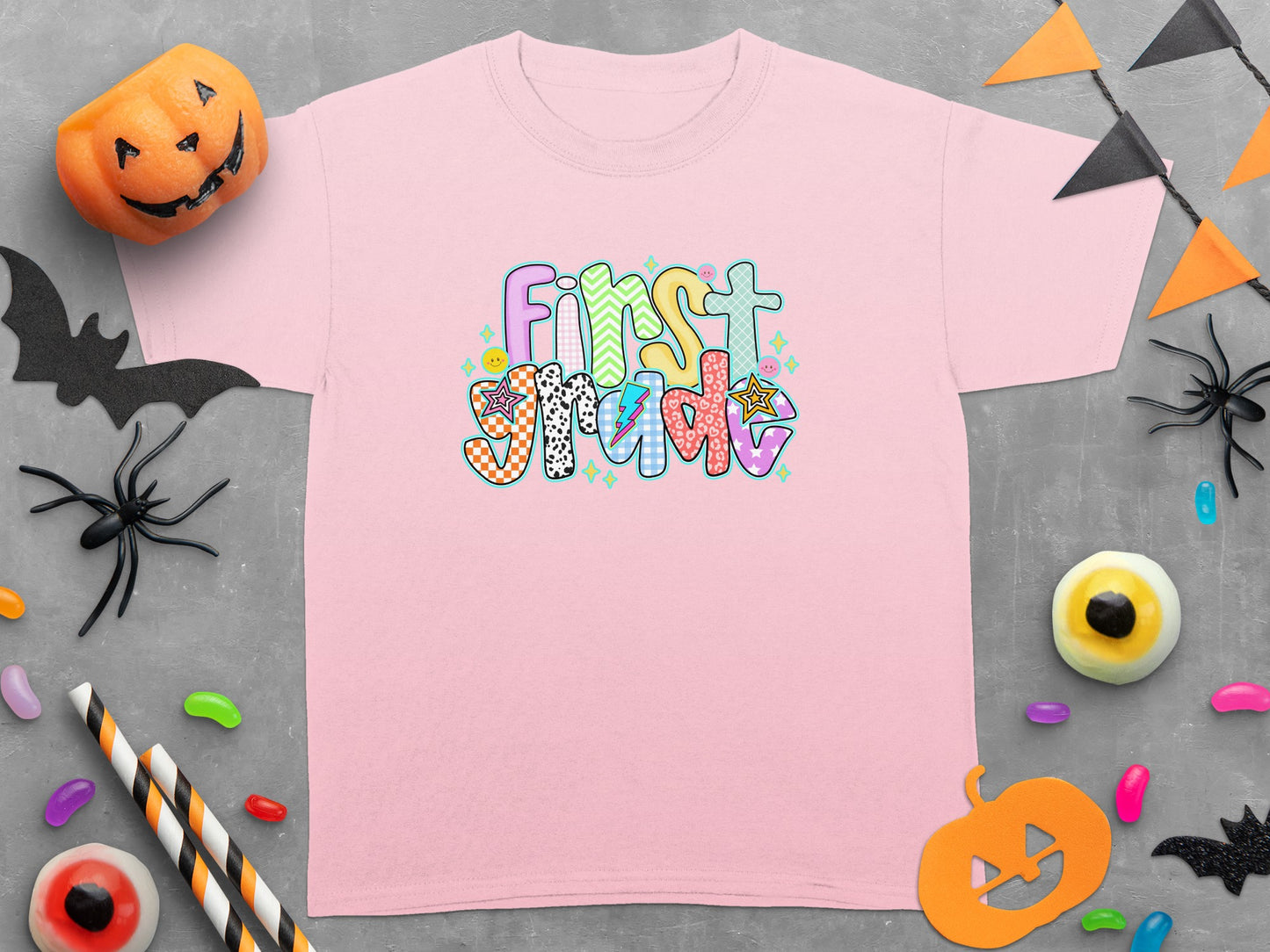 Pink t-shirt with "First Grade" text in colorful, patterned letters.