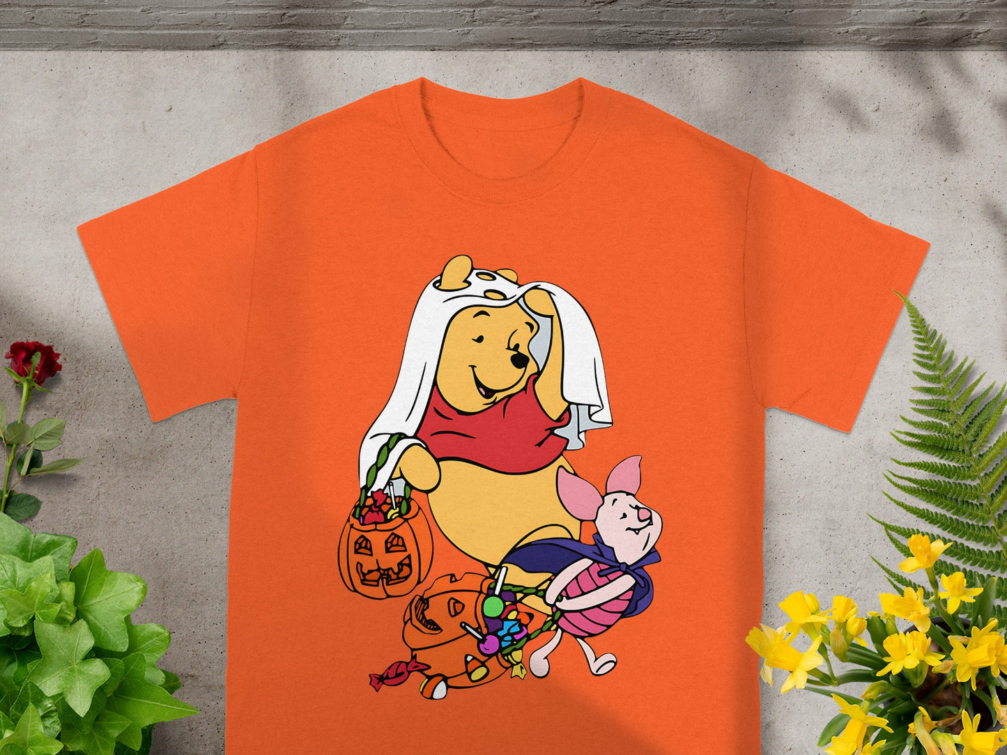 Winnie the Pooh and Piglet in Halloween costumes with candy on an orange t-shirt.