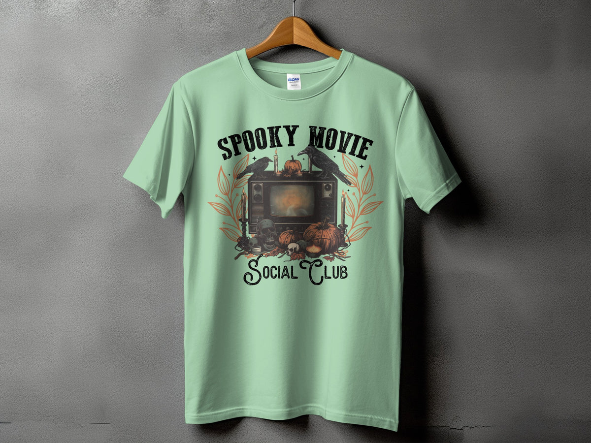 Light green t-shirt with "Spooky Movie Social Club" graphic featuring vintage TV and Halloween motifs.