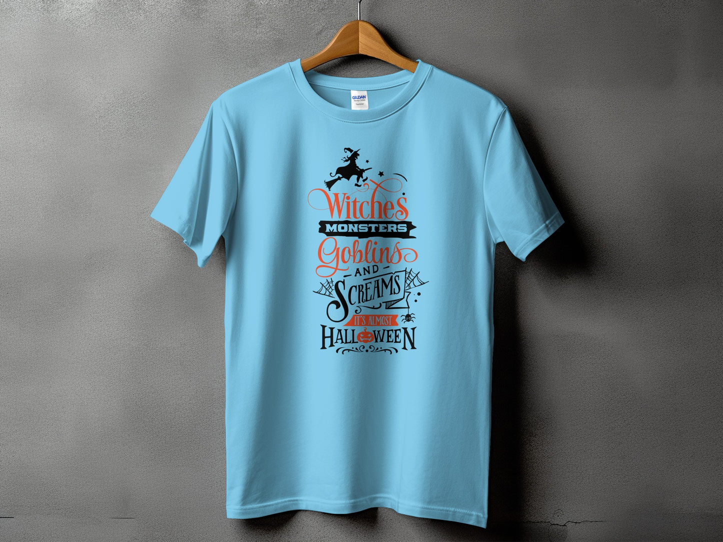Light blue t-shirt with "Witches, Monsters, Goblins, and Screams" Halloween text and witch graphic.