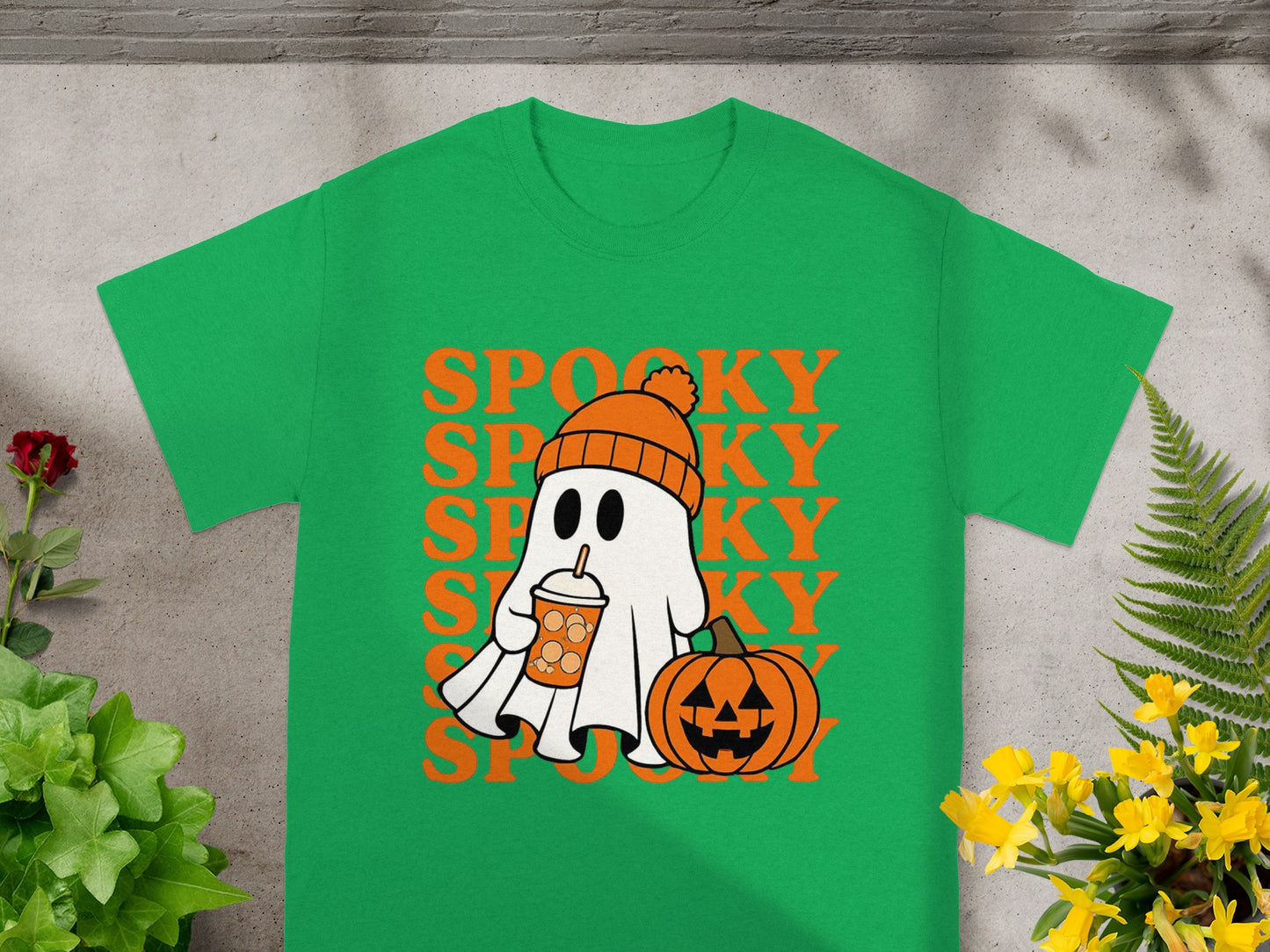 Green t-shirt with a cartoon ghost holding a pumpkin spice latte next to a jack-o'-lantern.
